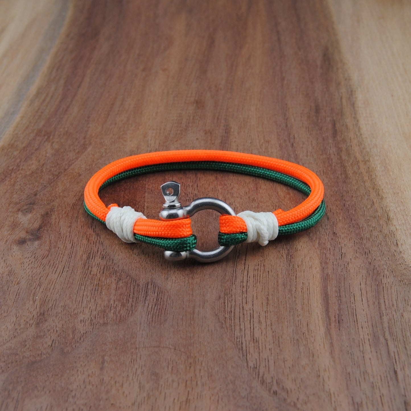 Bracelet with orange, green, and white straps on a wooden surface