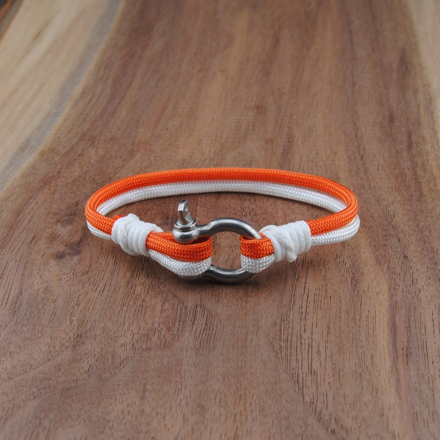Bracelet with orange and white cord on a wooden surface