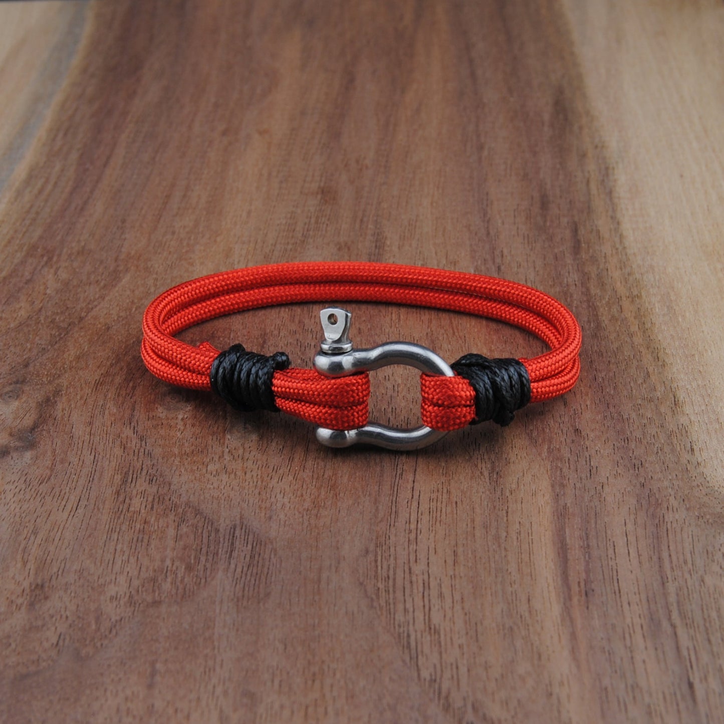 Red and black braided bracelet with a metal clasp on a wooden surface