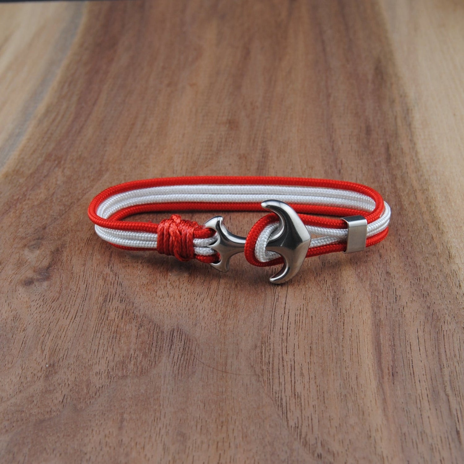 Bracelet with red and white cord and silver anchor clasp on a wooden surface
