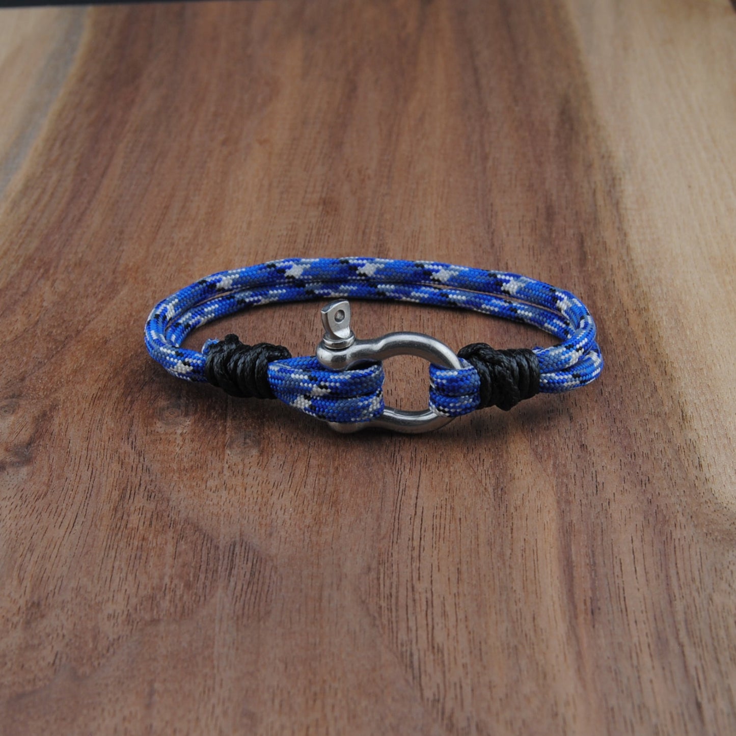 Blue and black braided bracelet with a metal clasp on a wooden surface