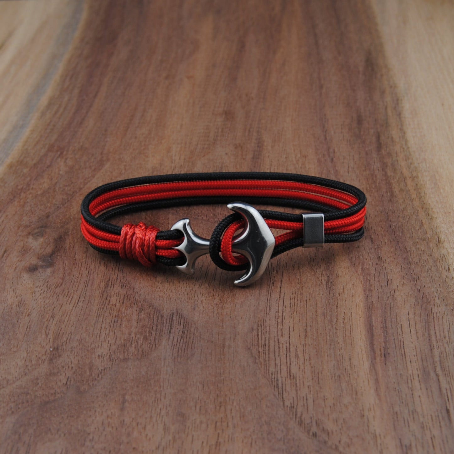 Red and black braided bracelet with a silver clasp on a wooden surface