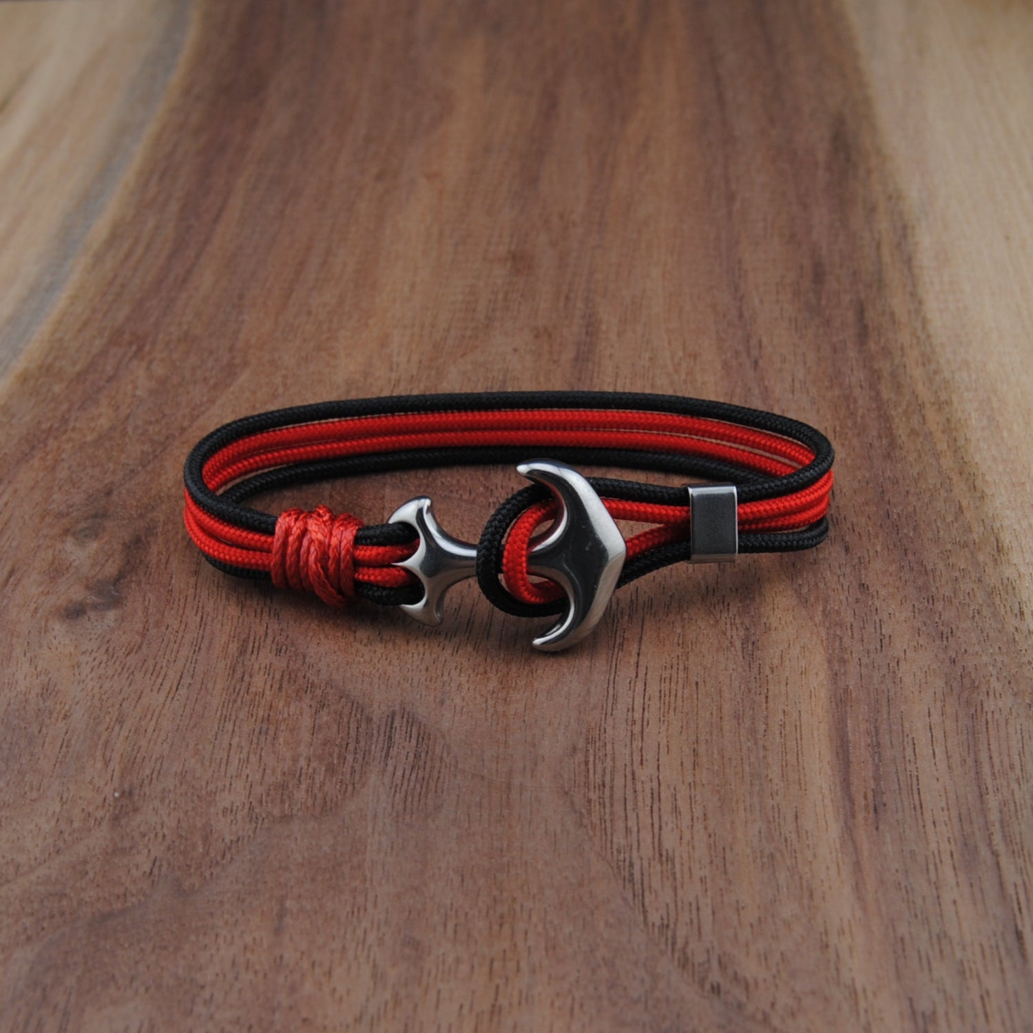 Red and black braided bracelet with a silver clasp on a wooden surface