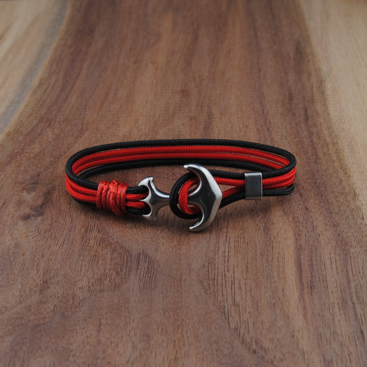 Red and black braided bracelet with a silver clasp on a wooden surface