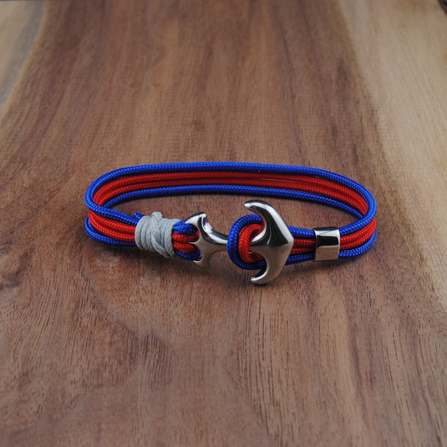 Bracelet with red and blue straps and a silver anchor clasp on a wooden surface