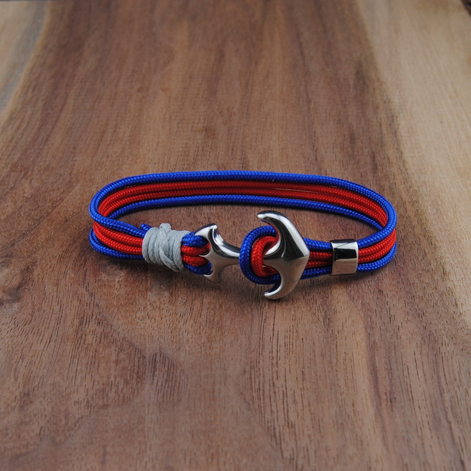 Bracelet with red and blue straps and a silver anchor clasp on a wooden surface
