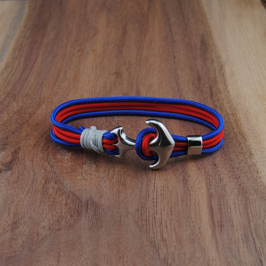 Bracelet with red and blue straps and a silver anchor clasp on a wooden surface