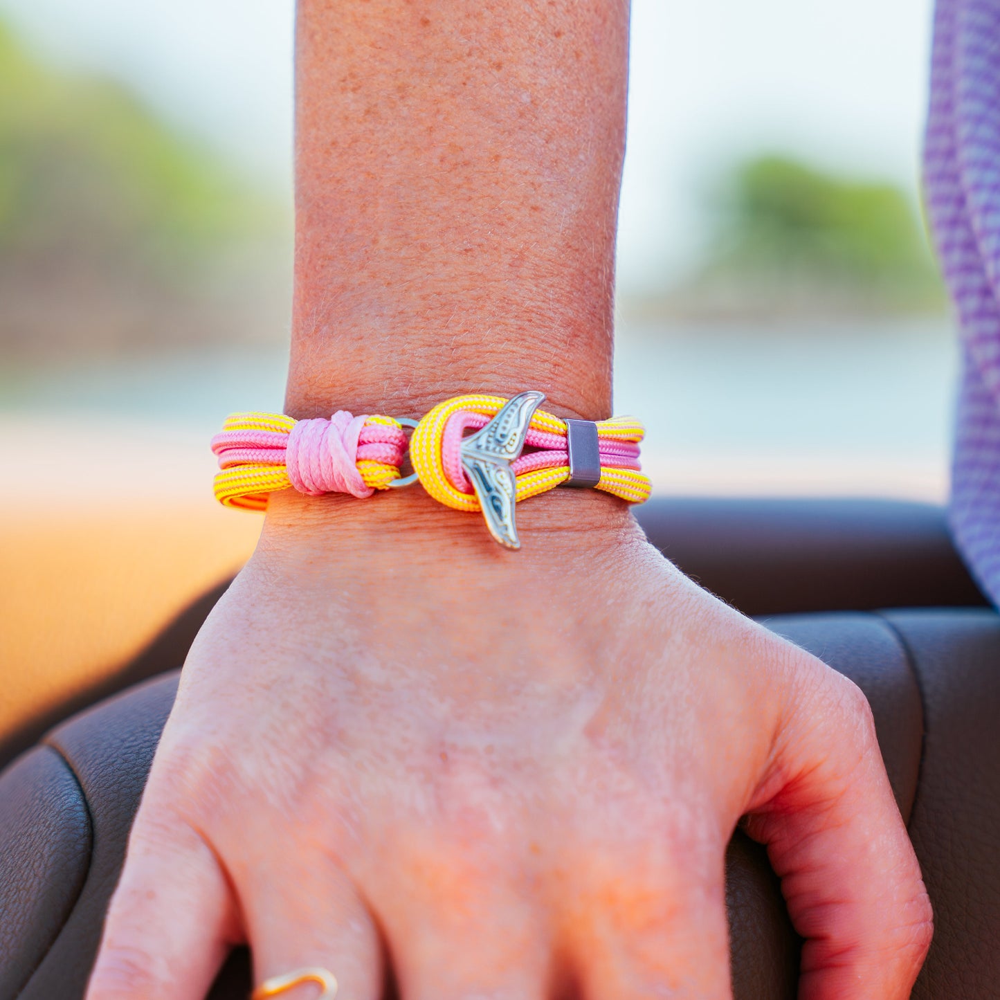 Hand wearing a colorful bracelet with a silver charm, blurred outdoor background