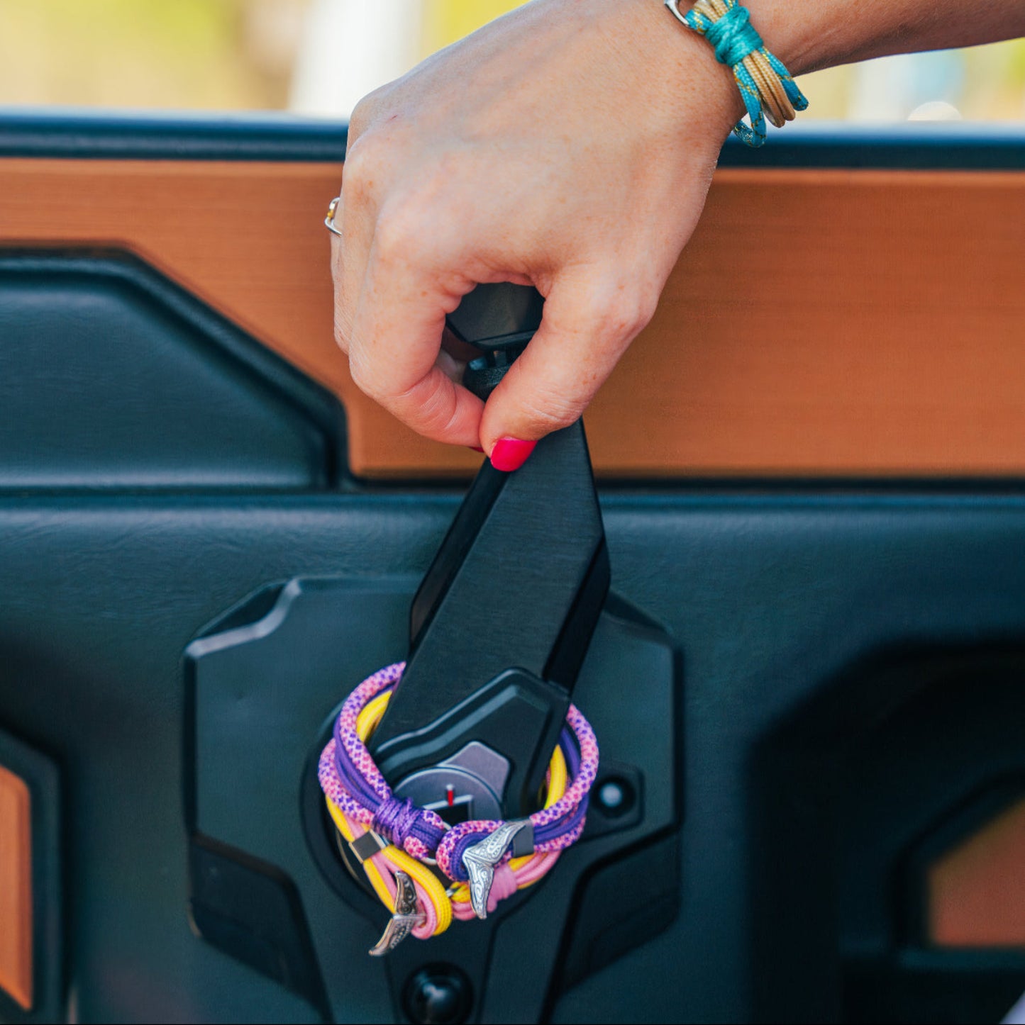 Hand opening a vehicle door with colorful keychain, blurred outdoor background