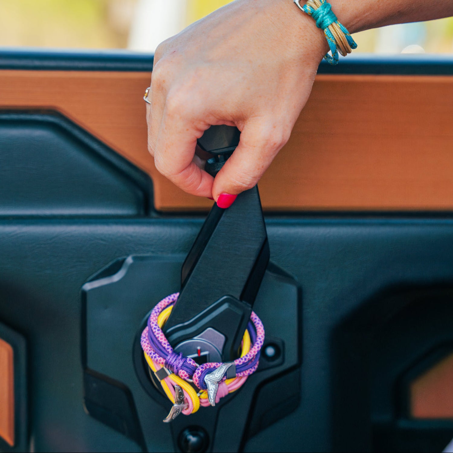 Hand opening a vehicle door with colorful keychain, blurred outdoor background