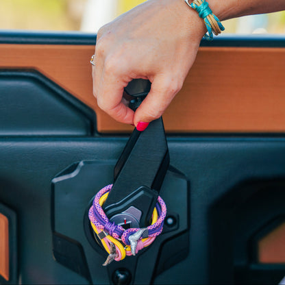 Hand opening a vehicle door with colorful keychain, blurred outdoor background