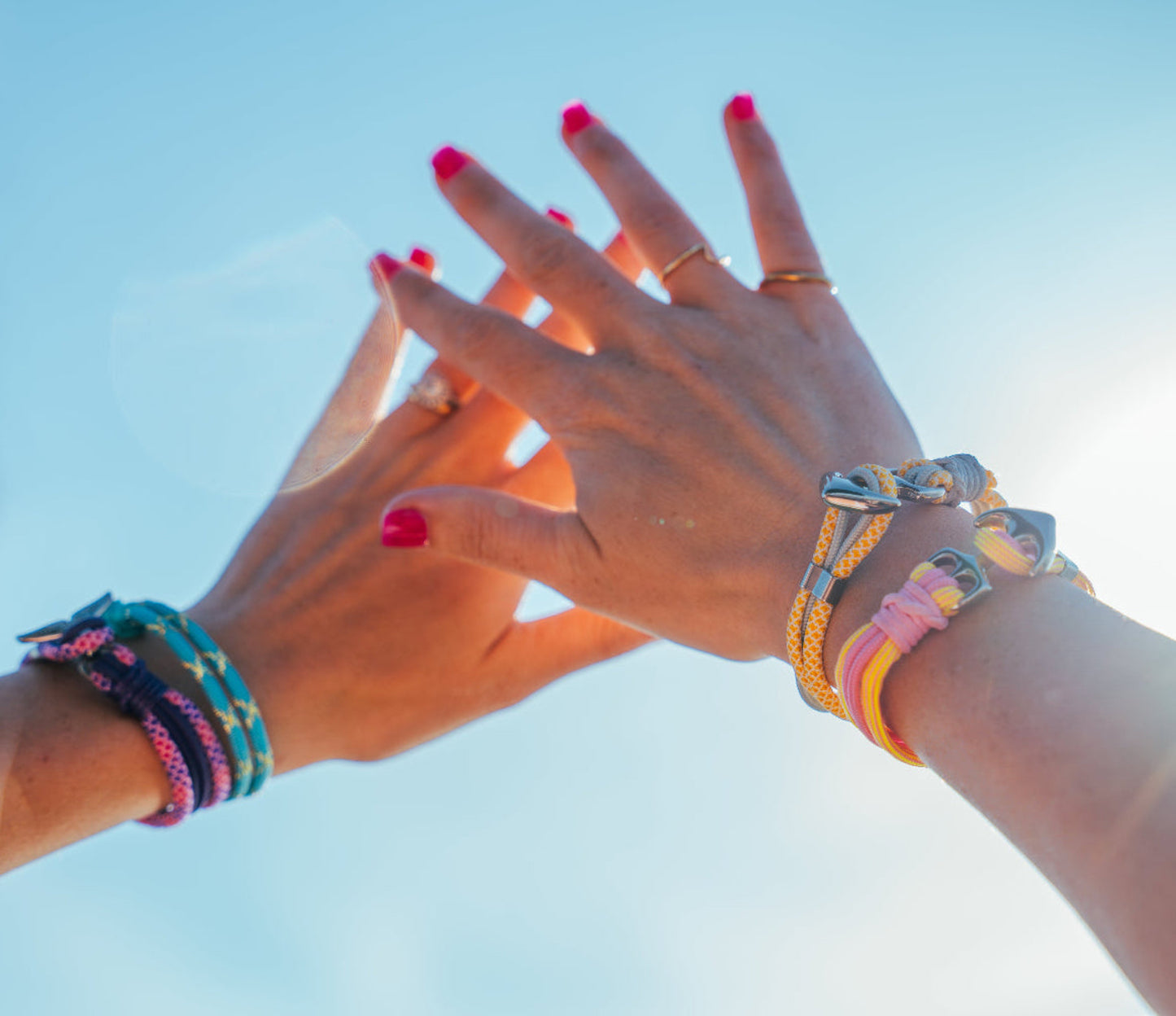 Two pairs of hands with colorful bracelets against a clear blue sky.