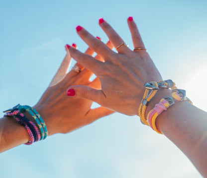 Two pairs of hands with colorful bracelets against a clear blue sky.
