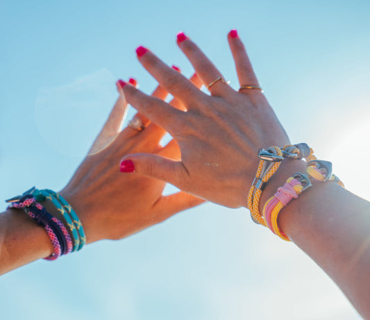 Two pairs of hands with colorful bracelets against a clear blue sky.