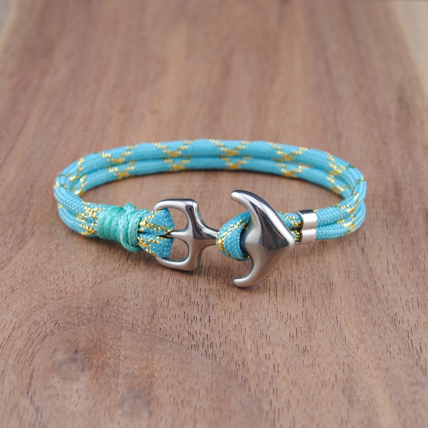 Turquoise braided bracelet with silver anchor clasp on a wooden surface