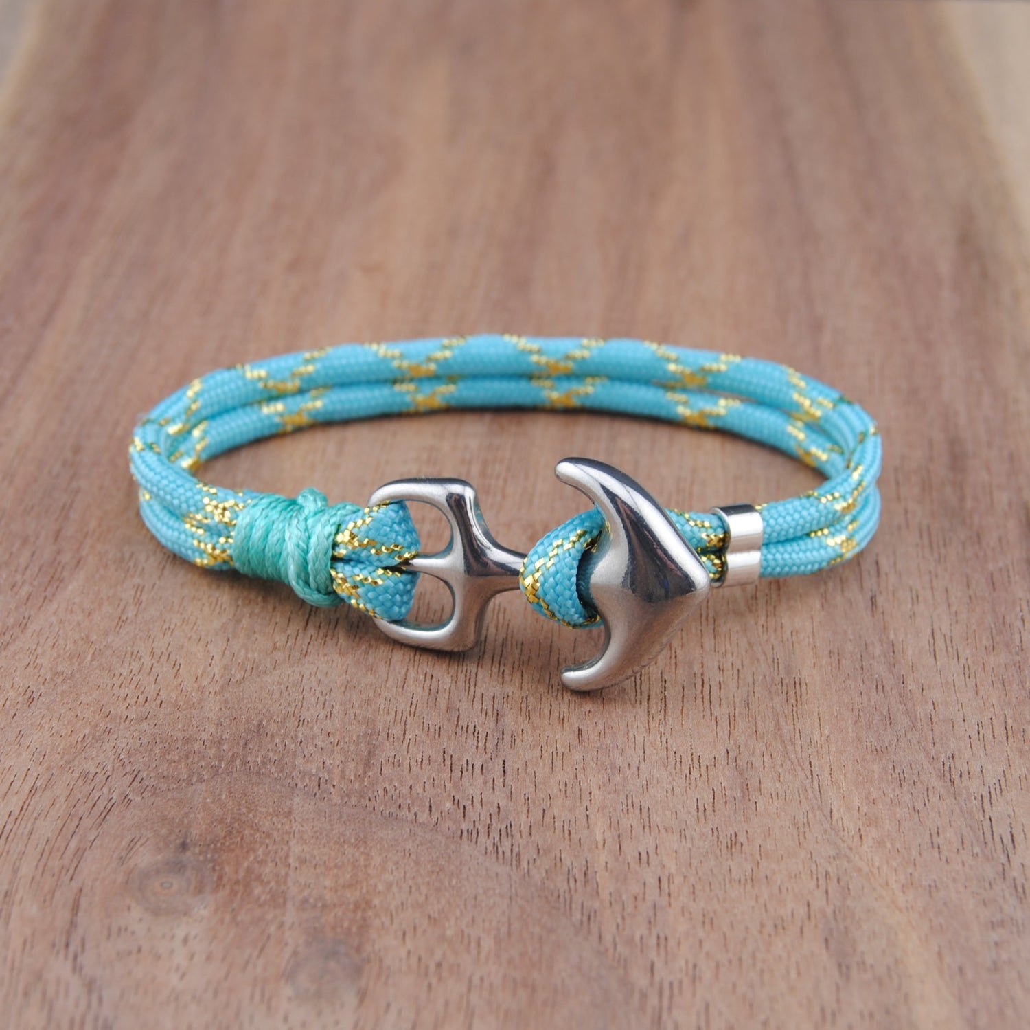 Turquoise braided bracelet with silver anchor clasp on a wooden surface