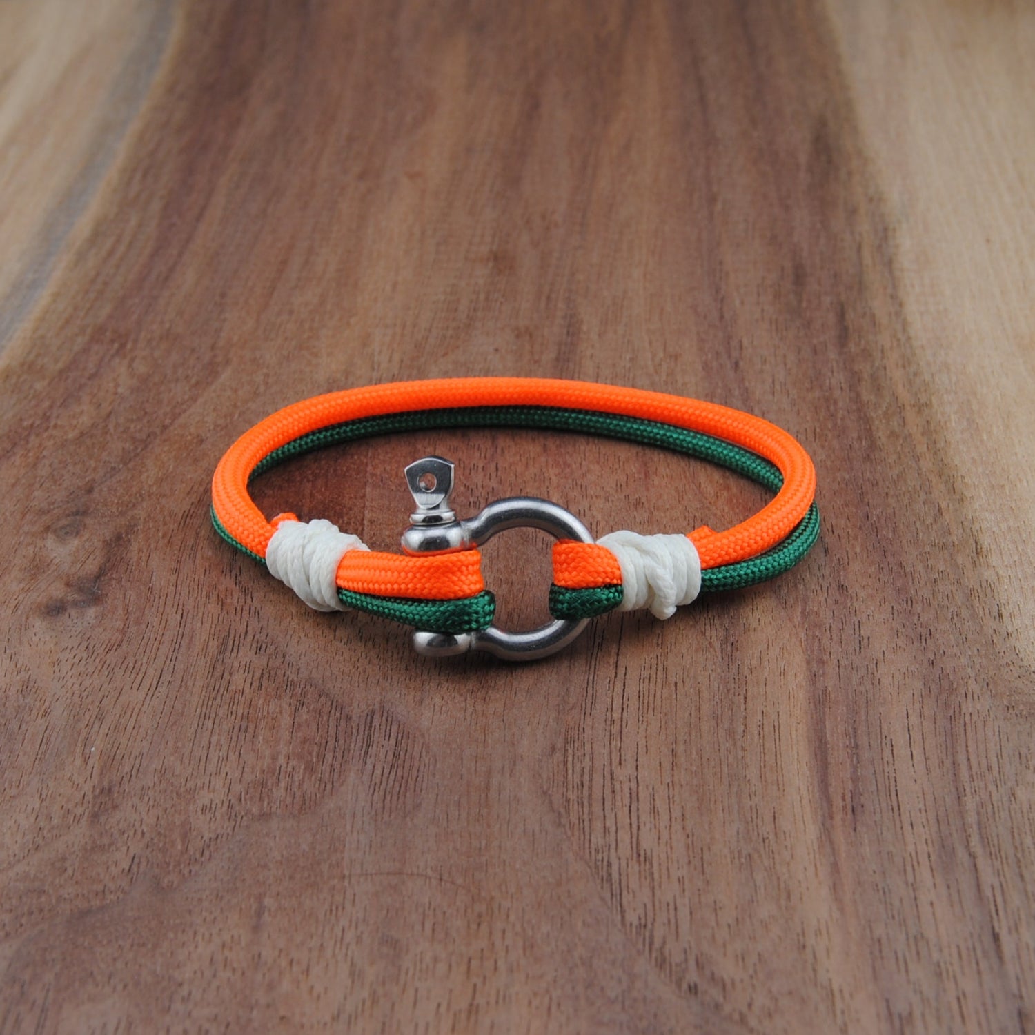 Bracelet with orange, green, and white straps on a wooden surface