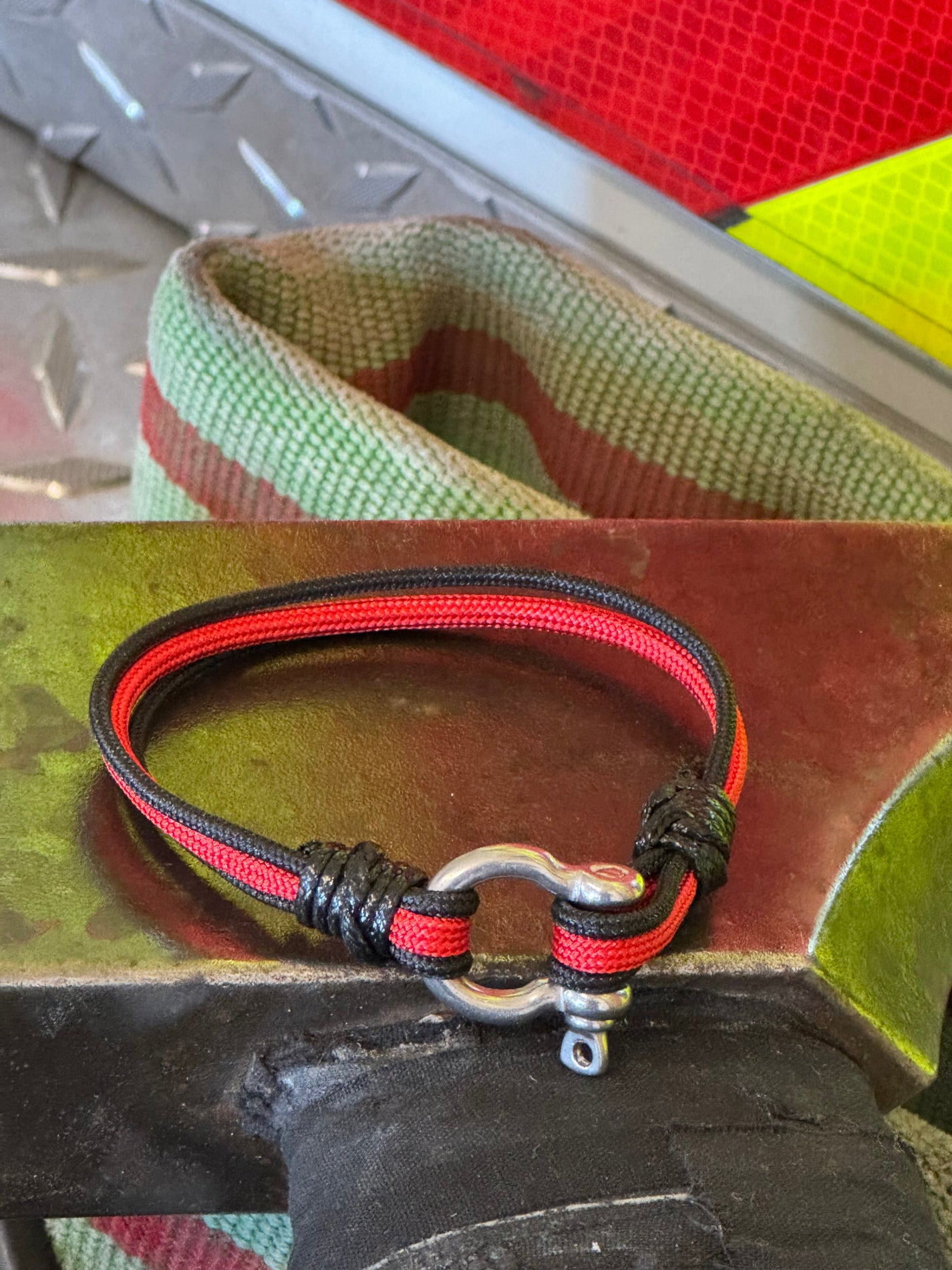 Close-up of a red and black paracord lanyard attached to a metal clip on a green surface.