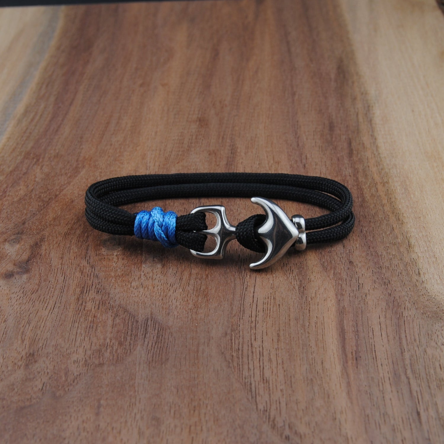 Black cord bracelet with a silver anchor clasp on a wooden surface