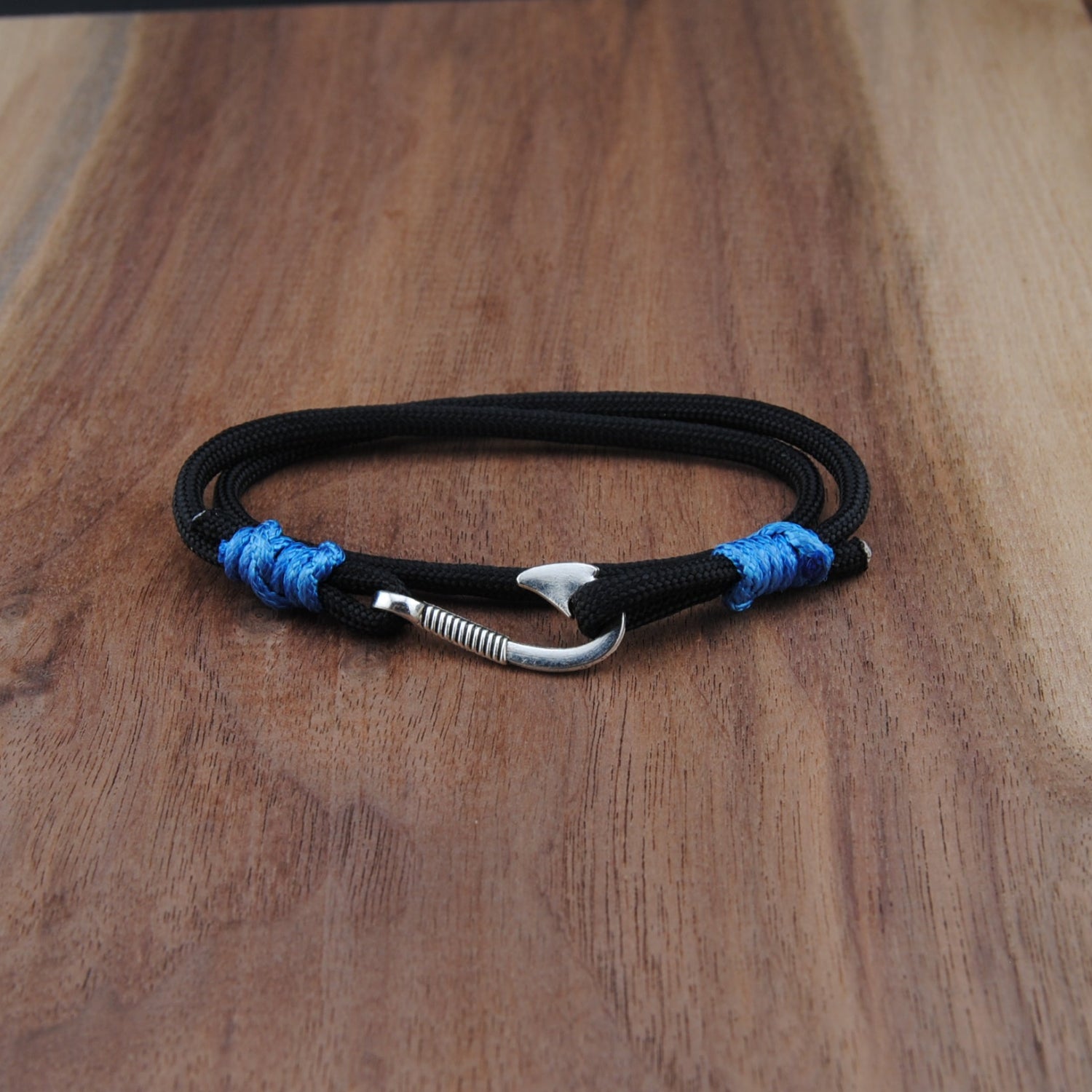 Black bracelet with blue accents and a silver hook clasp on a wooden surface