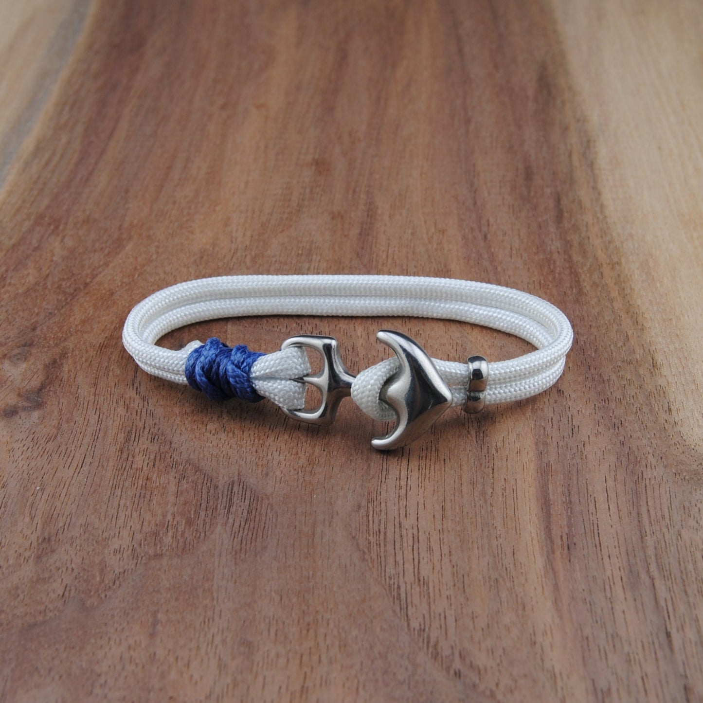 White bracelet with silver anchor clasp and blue bead on a wooden surface