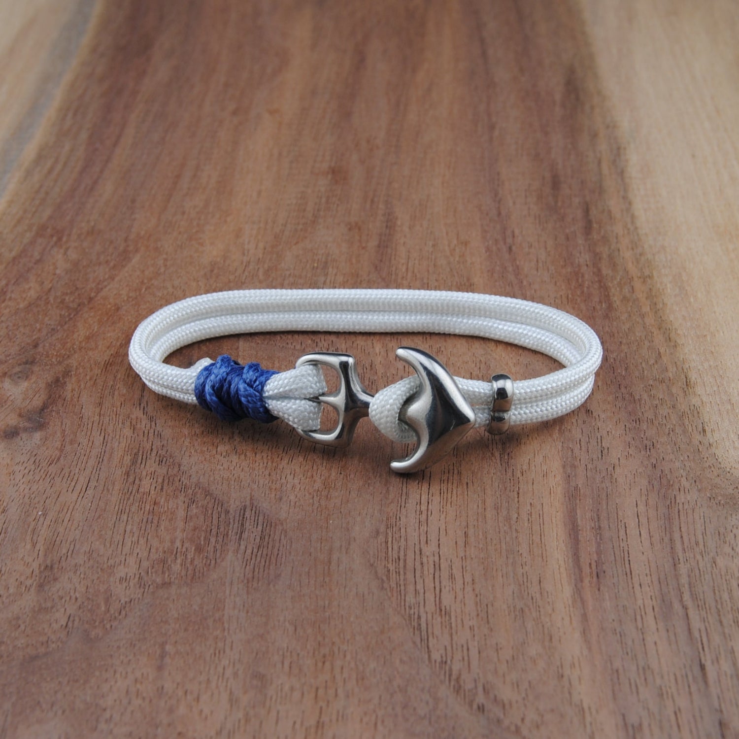 White bracelet with silver anchor clasp and blue bead on a wooden surface