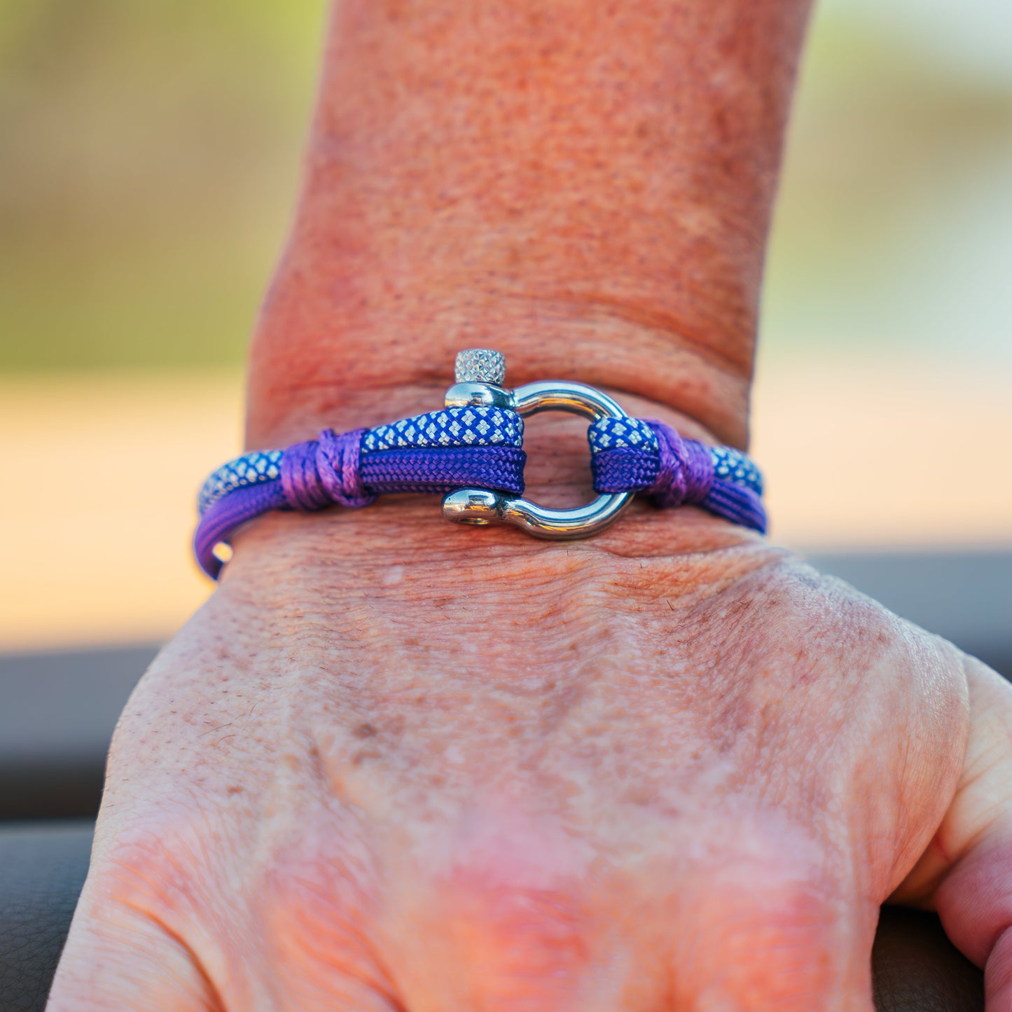Purple bracelet with a silver clasp on a person's wrist against a blurred natural background