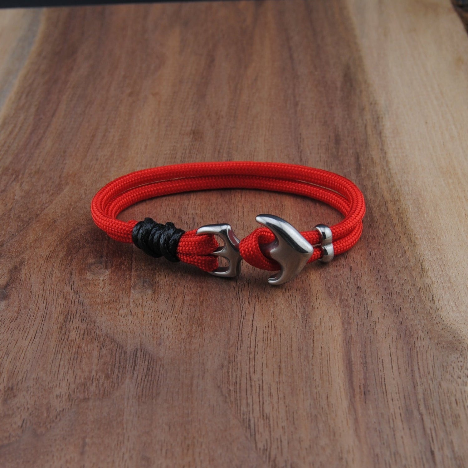 Red and black braided bracelet with metal clasp on a wooden surface