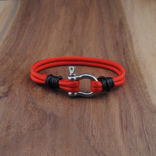 Red and black braided bracelet with a metal clasp on a wooden surface