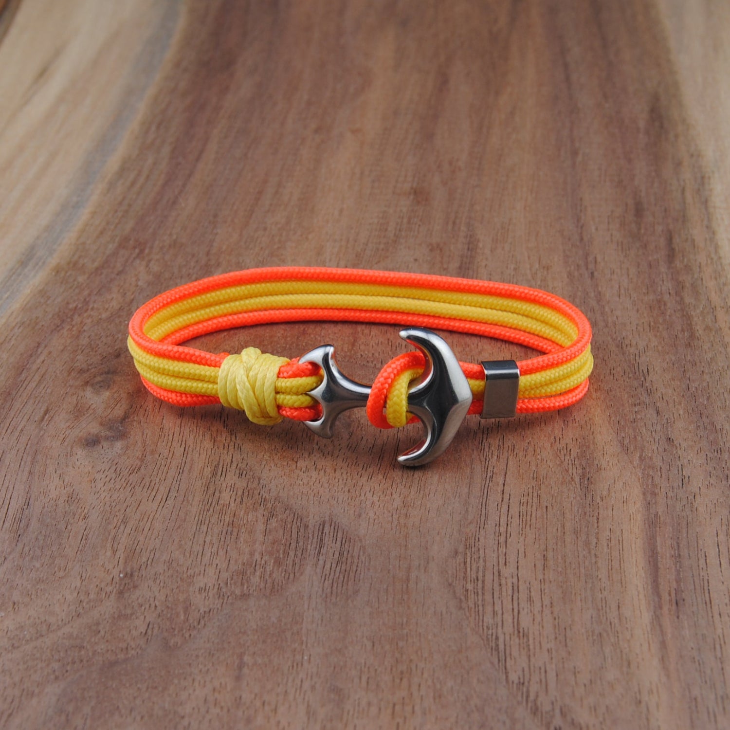 Neon orange and yellow bracelet with a silver anchor clasp on a wooden surface