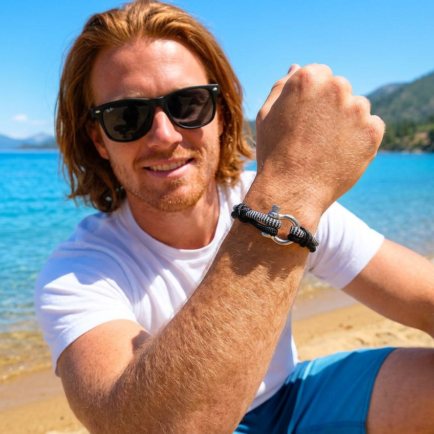 Man on a beach wearing sunglasses and a white t-shirt with blue shorts, with a scenic background.