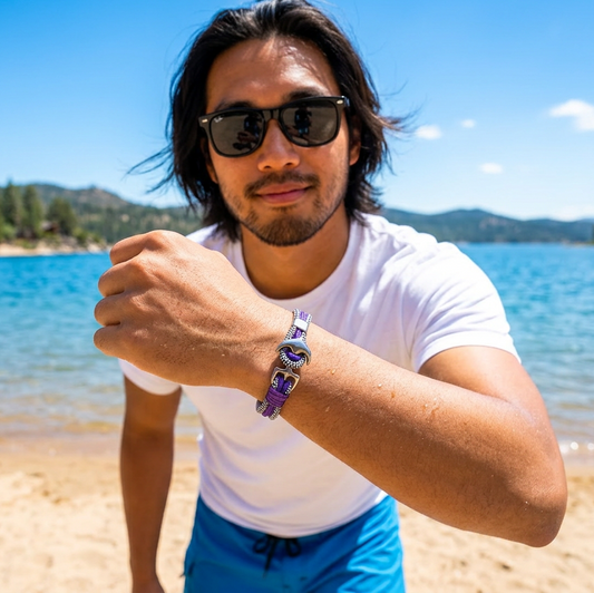 Man wearing sunglasses and a Bracelet on a beach with a lake and mountains in the background